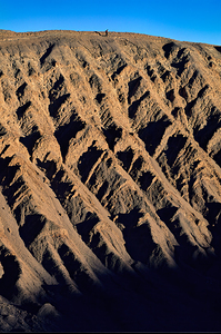 Hiker traverses a dramatic shadowed desert landscape. by Marco Brivio