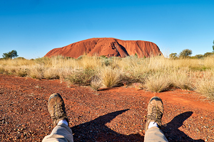 Persons feet in hiking boots in front of Uluru.