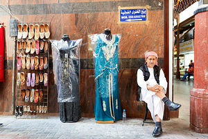 Man sits by shoes and dresses while relaxing in Dubai market