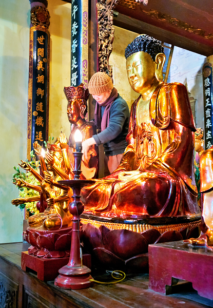 Buddhist monk praying near golden statues in Hanoi by Marco Brivio