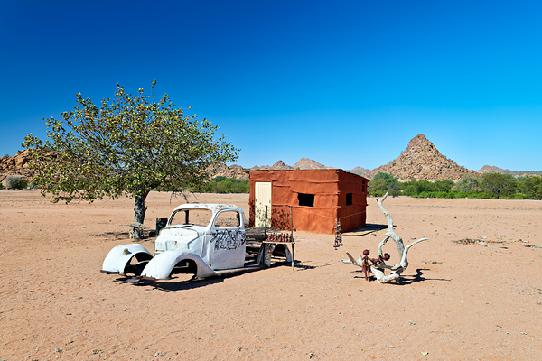 Classic car wreck in Namibias desert landscape near a structure Print