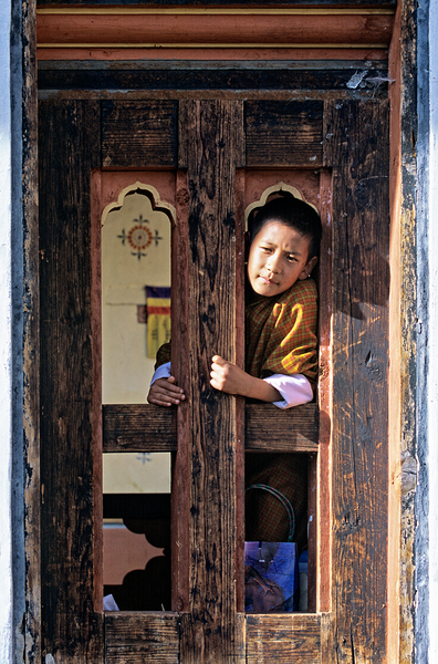 Bhutanese child peeking from ornate wooden window. by Marco Brivio