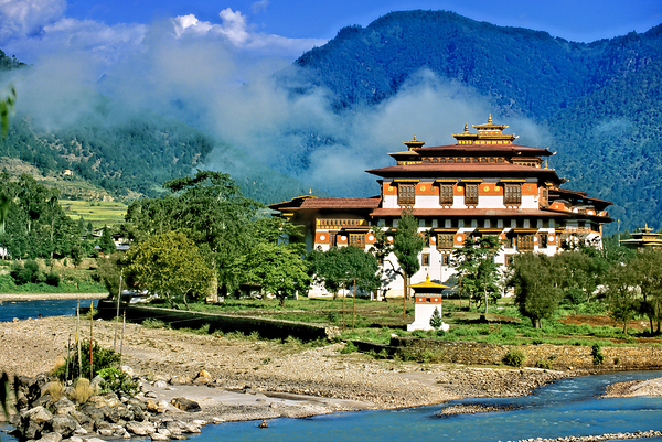 Bhutanese monastery by river with misty mountains. by Marco Brivio