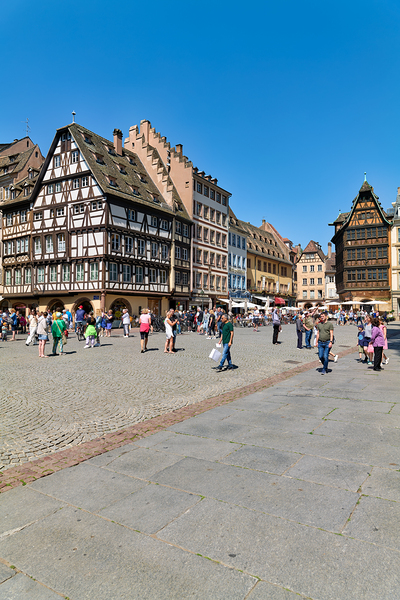 Visitors gather in busy square with colorful houses in Strasbour by Marco Brivio