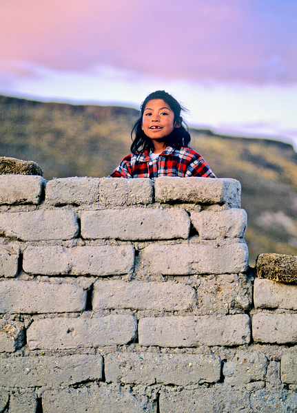 Young girl smiles over stone wall at sunset. Print