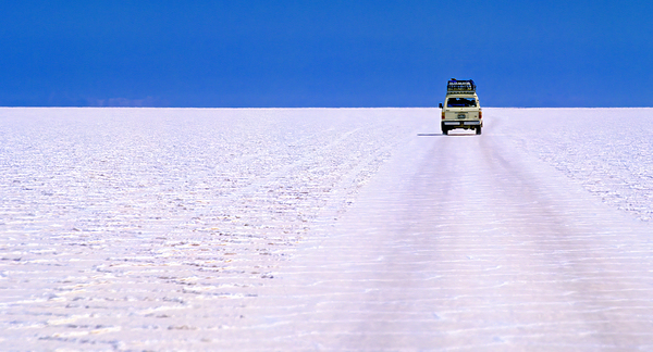 Van driving across vast white salt flat under blue sky. Print