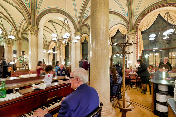 Man playing piano in an ornate bustling cafe. Print