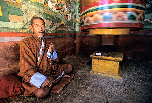 Bhutanese man with prayer beads and spinning prayer wheel. by Marco Brivio