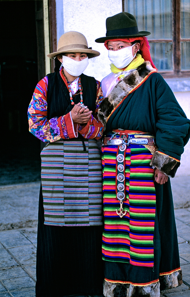 Masked individuals in traditional clothing hold hands in Tibet by Marco Brivio