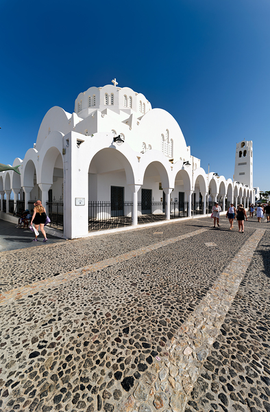 White church cobblestone path and people under a blue sky. by Marco Brivio