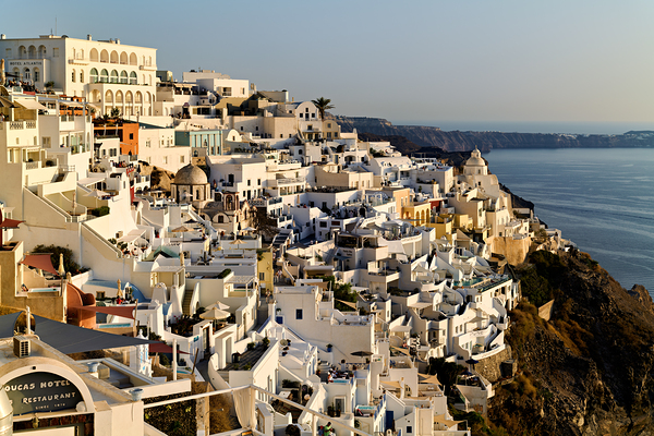 Santorinis white buildings cascade down cliff to the sea. Print