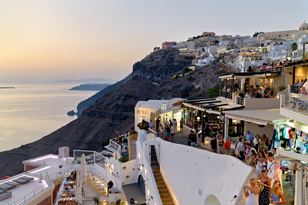 Santorini cliffside town with restaurants and people enjoying th Print