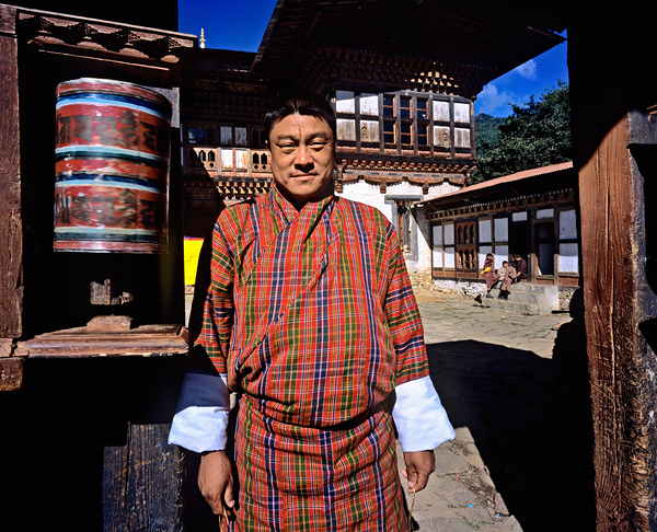 Bhutanese man in traditional gho with prayer wheel. by Marco Brivio