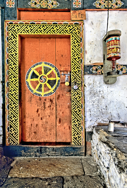 Colorful Bhutanese door with Dharma wheel and prayer wheel. by Marco Brivio