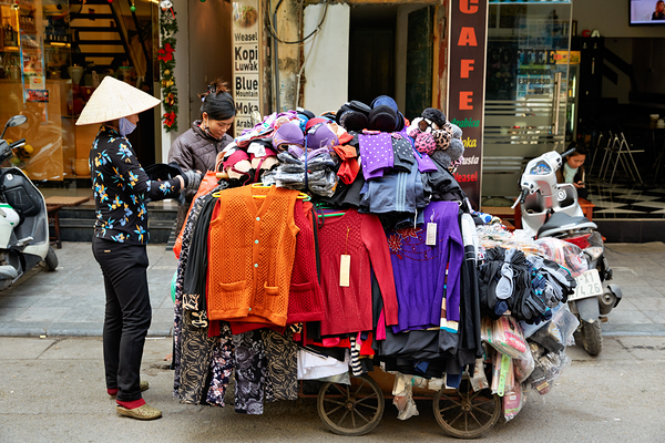 Market scene in Hanoi with a man selling clothes on a cart by Marco Brivio