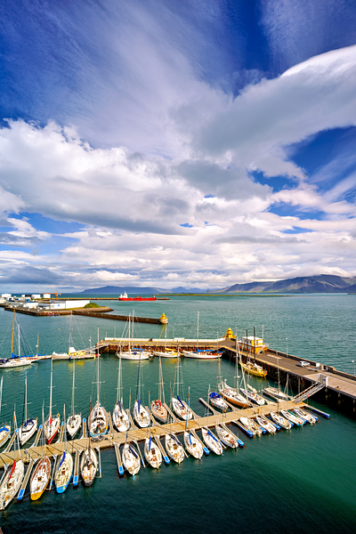 Sailboats docked in Reykjavik harbor under cloudy sky by Marco Brivio