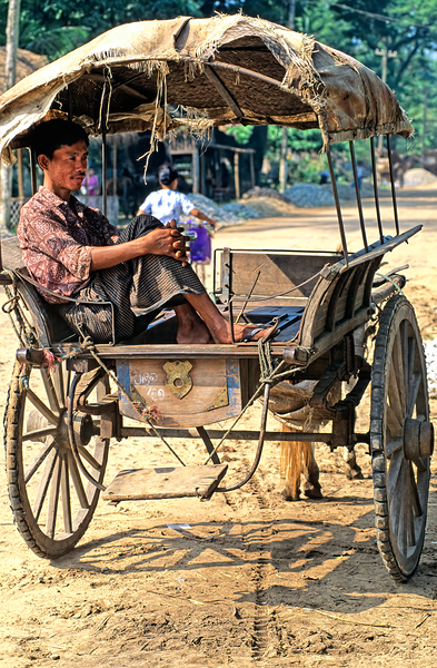 Man rests on cart in Myanmar during warm daytime Print