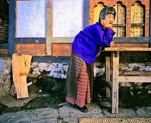 Smiling elderly woman in traditional dress leaning on wooden tab by Marco Brivio