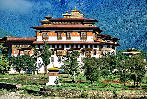 Majestic Bhutanese dzong amidst green mountains and trees. by Marco Brivio
