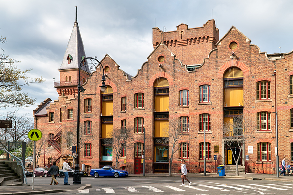 Historic brick building with a tower and people walking. Print