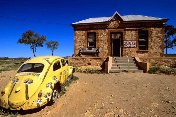 A painted yellow Beetle outside a rural stone gallery. Print