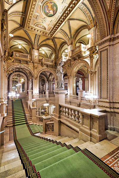 Ornate grand staircase with green carpet and classical statues. Print
