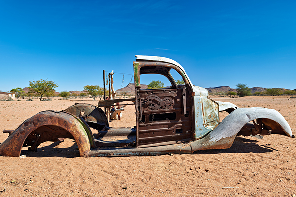 Classic car wreck rests in the Namib desert under a clear sky Print