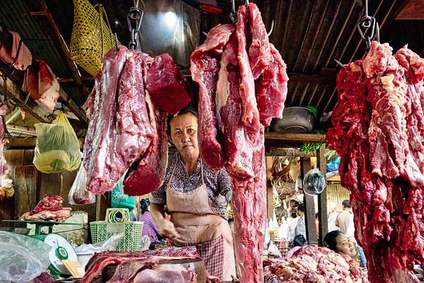 Woman selling raw meat in a bustling market. Print