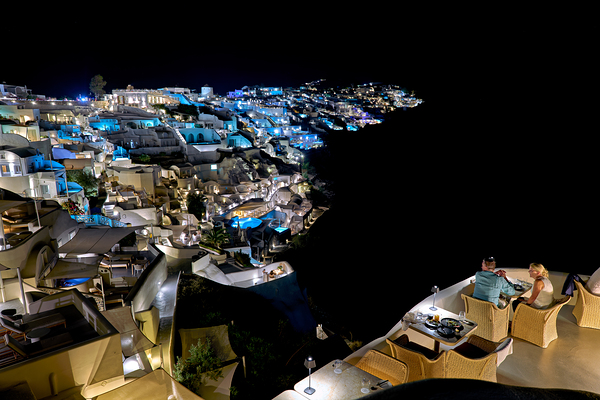 Illuminated cliffside town at night couple enjoying dinner. Print
