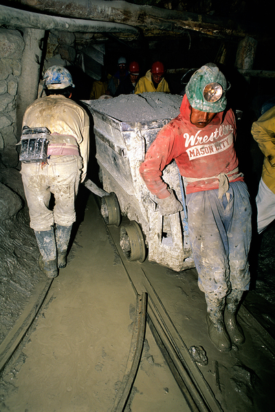 Miners pushing a loaded cart through a muddy underground mine. Print