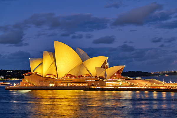 Sydney Opera House illuminated at dusk with harbor lights. Print
