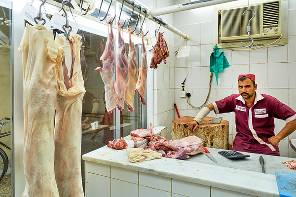Butcher works in meat market in Dubai with hanging meat Print