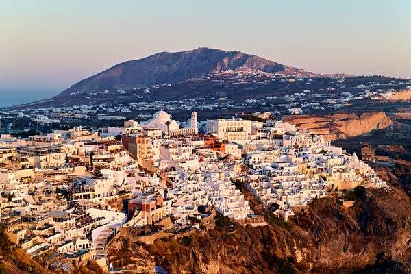 Santorini cliffside town at sunset with mountain backdrop. Print