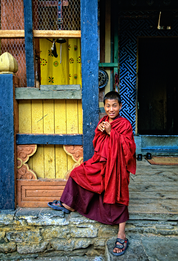 Smiling young monk in red robes at colorful traditional building  Print