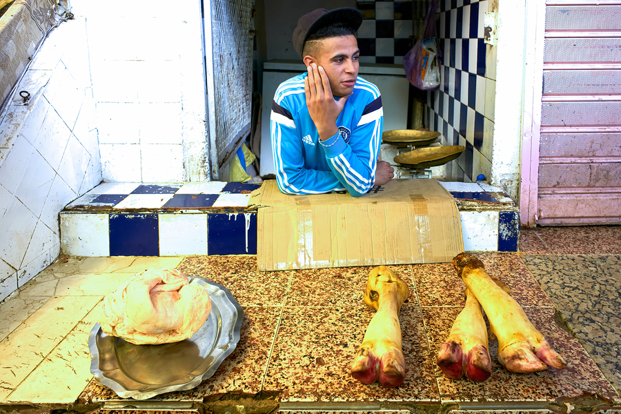 Butcher in Meknes souk interacts with customers during market ho  Print