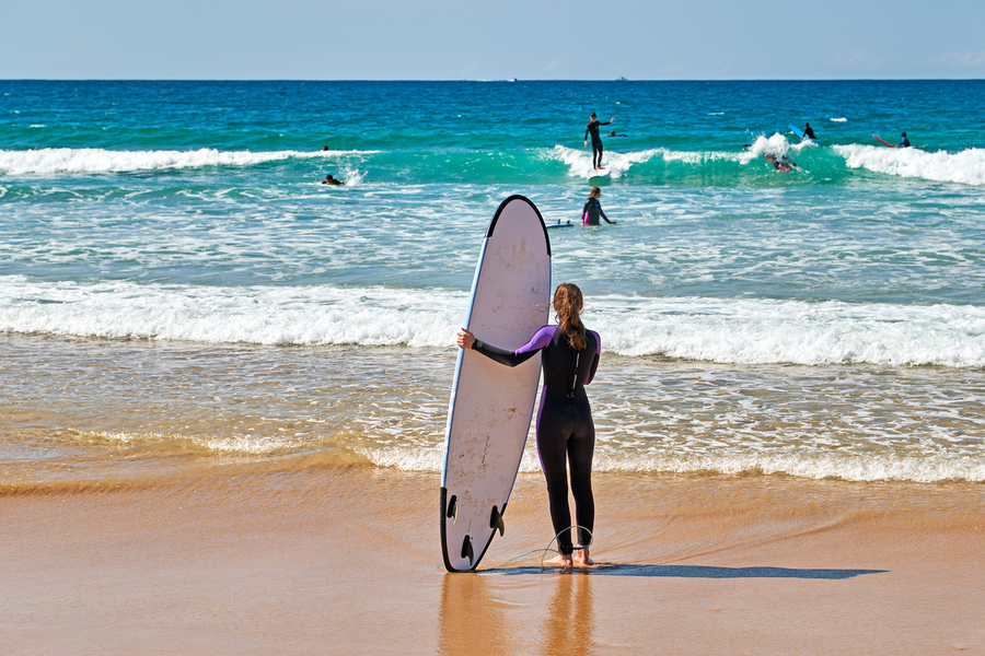 Surfer girl with surfboard on beach watching waves  Print