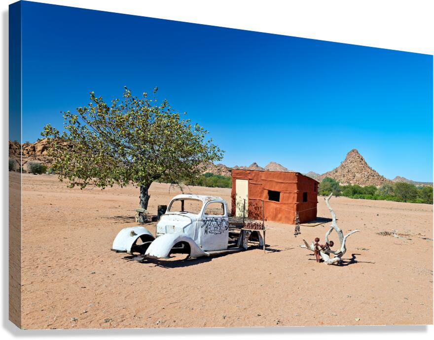 Classic car wreck in Namibias desert landscape near a structure Canvas Print