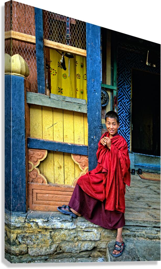 Smiling young monk in red robes at colorful traditional building Canvas Print