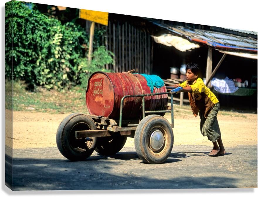 Boy pushes a cart down the street in Myanmar during the day Canvas Print