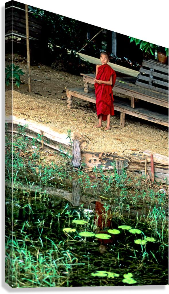 Young monk stands by water in Myanmar during daytime Canvas Print