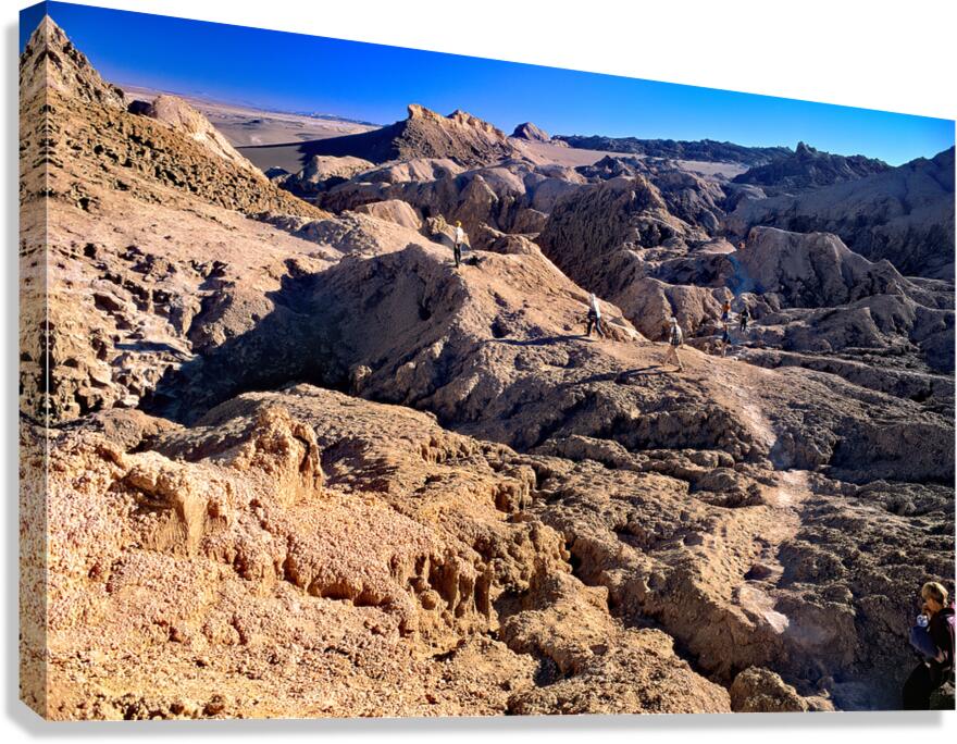 Hikers traverse a vast arid rocky desert landscape. Canvas Print