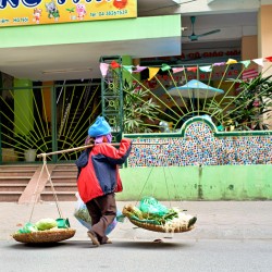 Woman carries baskets on busy street in Hanoi during daytime