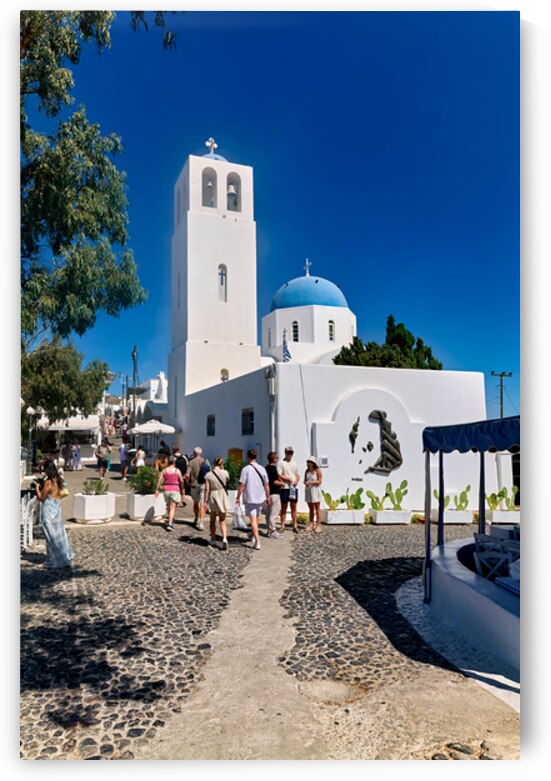 Greek village street with white church blue dome and tourists. by Marco Brivio