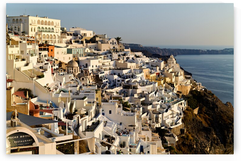 Santorinis white buildings cascade down cliff to the sea. by Marco Brivio