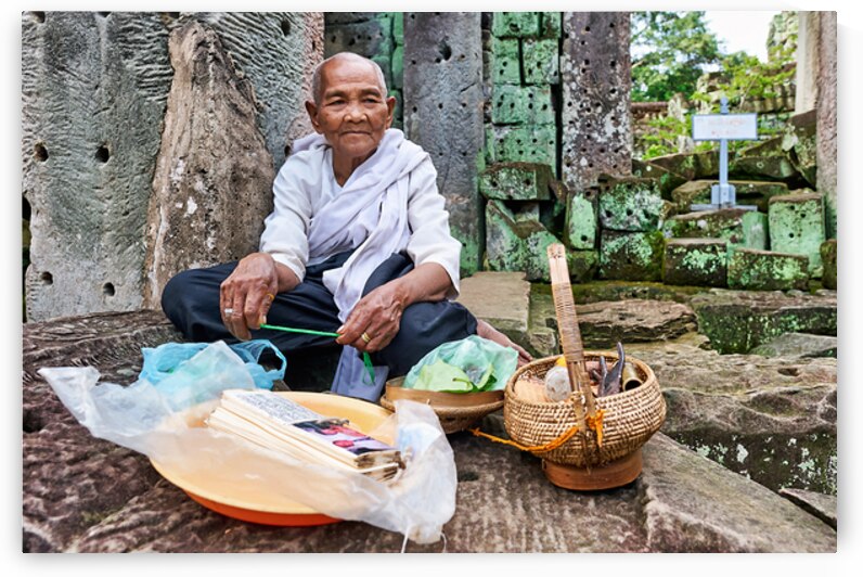 Elderly person selling goods at ancient temple ruins. by Marco Brivio