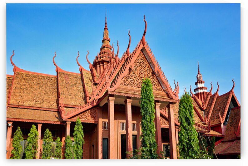 Red roofed Cambodian temple with ornate details against blue sky by Marco Brivio