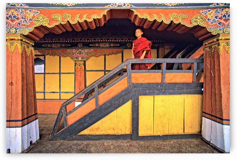 Young monk in red robes on colorful temple staircase. by Marco Brivio