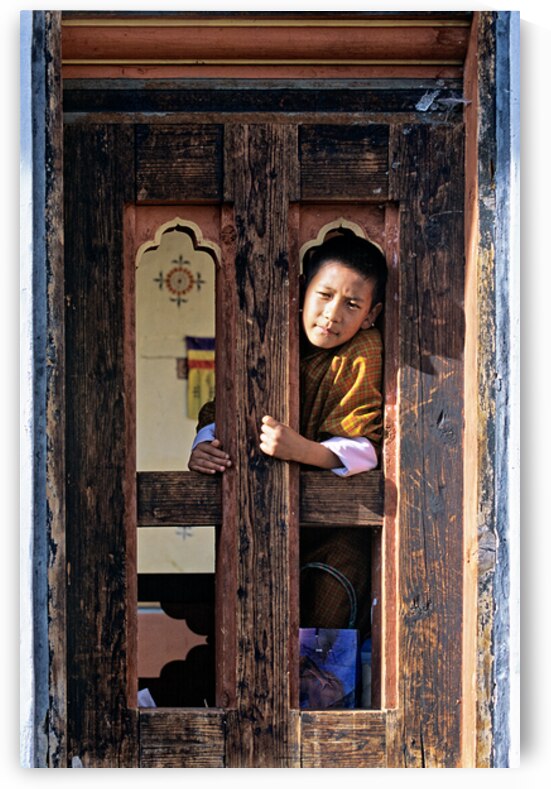Bhutanese child peeking from ornate wooden window. by Marco Brivio