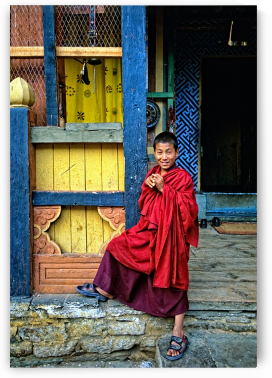 Smiling young monk in red robes at colorful traditional building by Marco Brivio