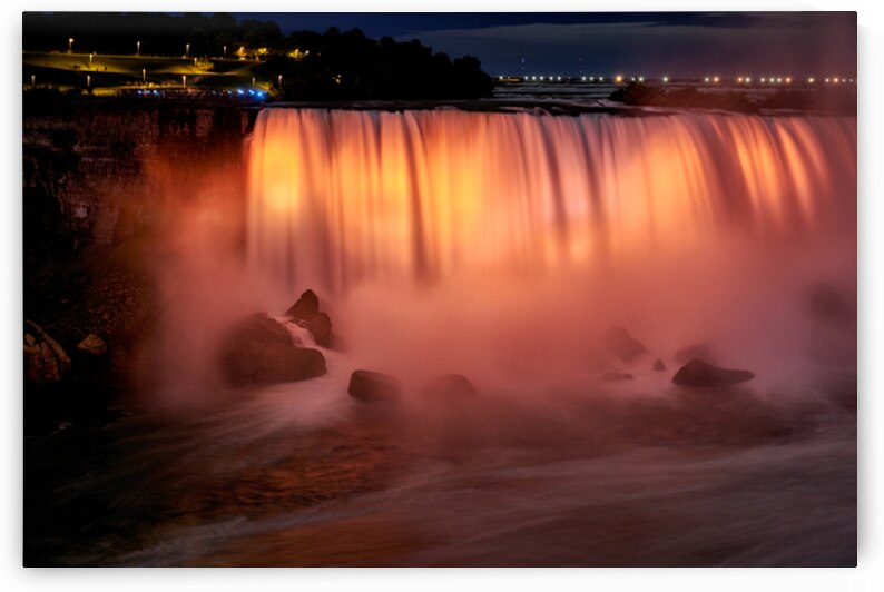 Niagara Falls illuminated orange at night. by Marco Brivio